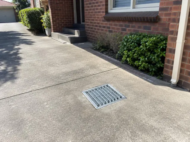 Concrete driveway with a metal drain grate beside a brick house in Bexley