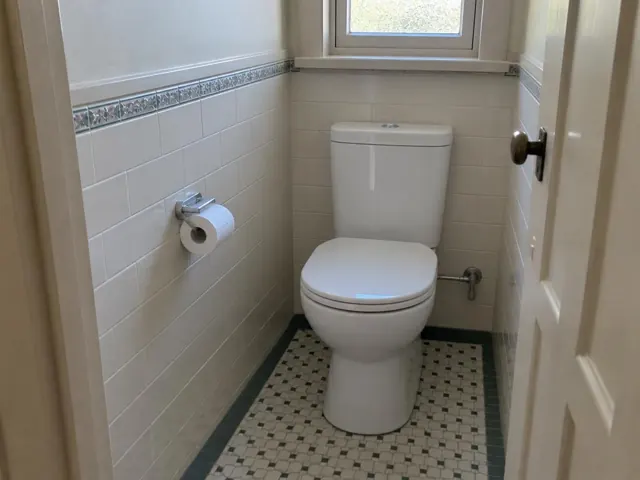 Clean toilet in a tiled small bathroom with window and mosaic floor in Arncliffe