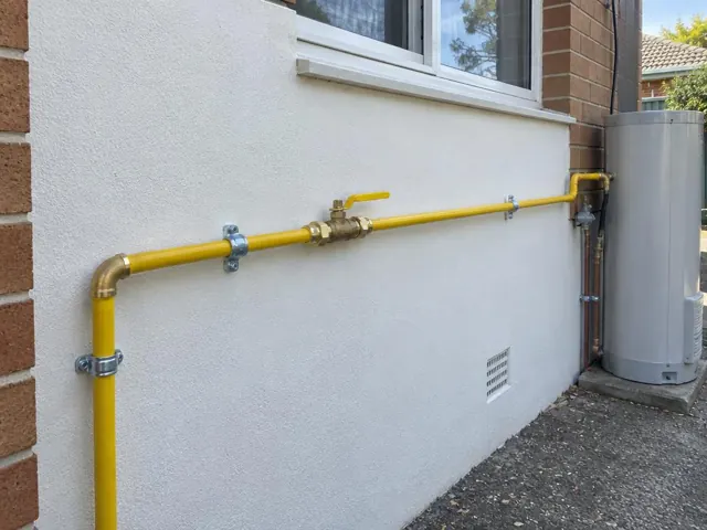 Yellow gas pipe and fittings on an exterior brick and render wall beside a window in Kingsgrove
