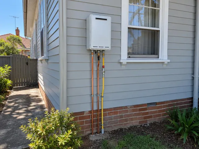 Wall-mounted hot water unit with exposed copper and gas pipes beside a window on a house exterior in Bexley